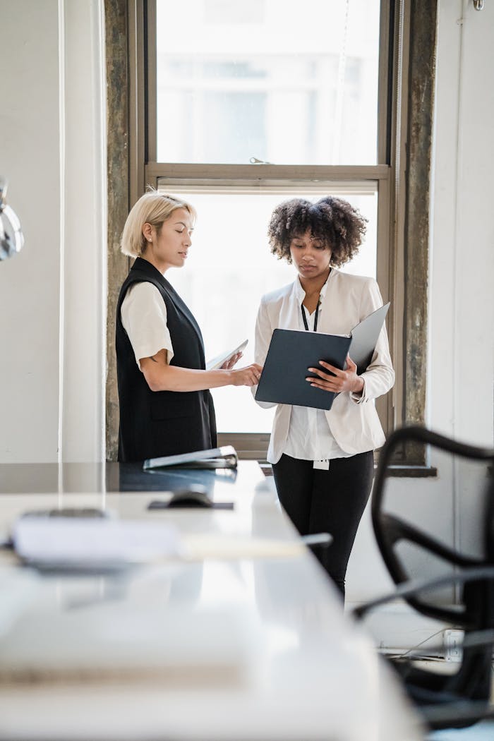 who-we-are Two businesswomen discussing documents in a modern office setting.