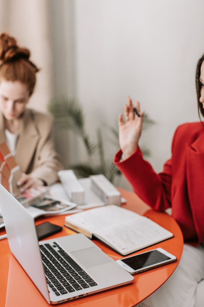 Two women having a discussion at a table with laptops and notes.